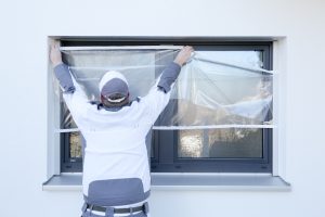 Ein Maler klebt mit Folie von Klauss-Klebeband ein Fenster ab