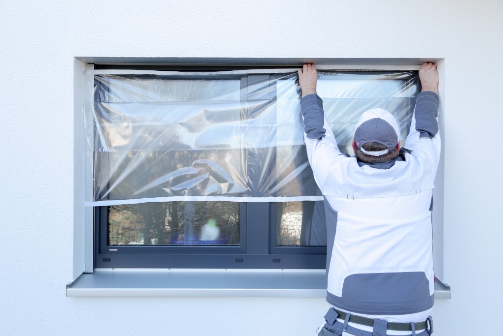 Ein Maler klebt mit Folie von Klauss-Klebeband ein Fenster ab