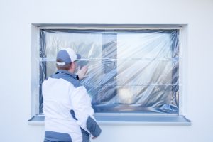 Ein Maler klebt mit Folie von Klauss-Klebeband ein Fenster ab